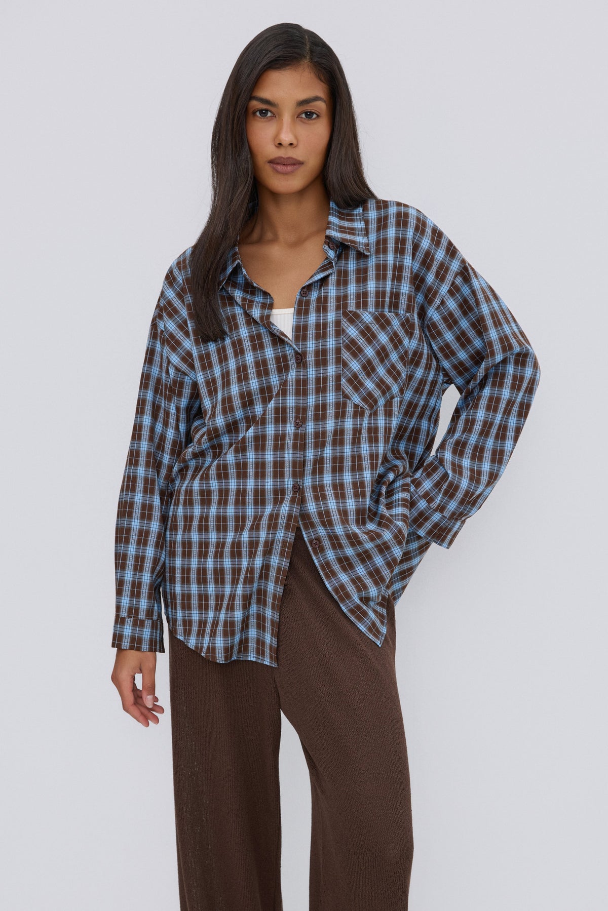 Nahaufnahme des Models in der lässig geöffneten blau-braun karierten Oversize-Hemdbluse