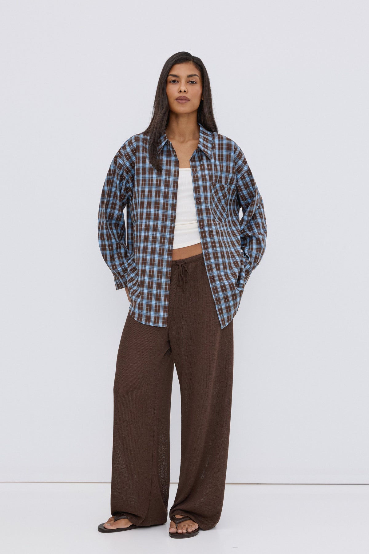 Frontansicht des Models, das die blau-braune Karo-Bluse über einem weißen Top und braunen Hosen trägt