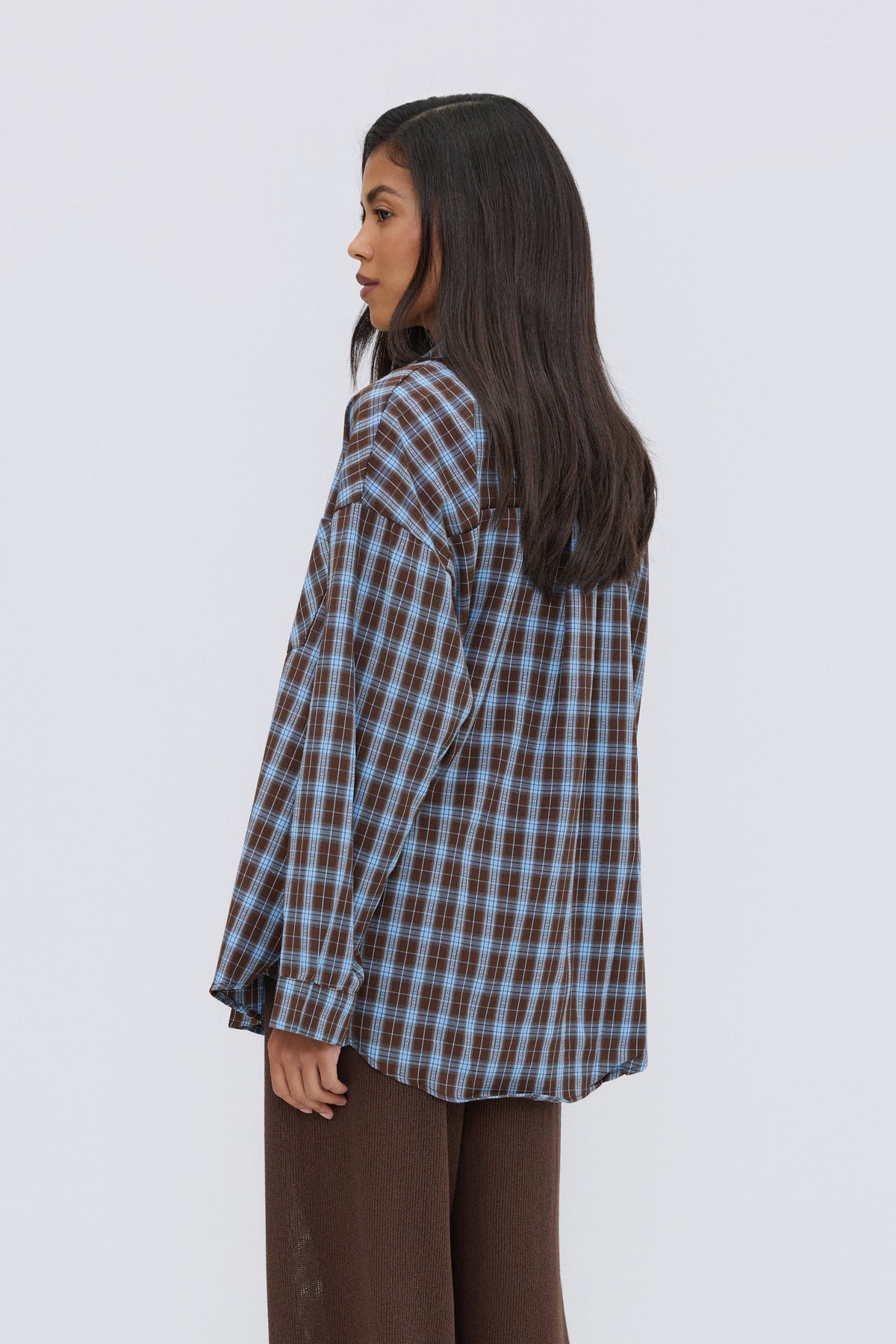 Rückansicht des Models in der überschnittenen, blau-braun karierten Oversize-Bluse