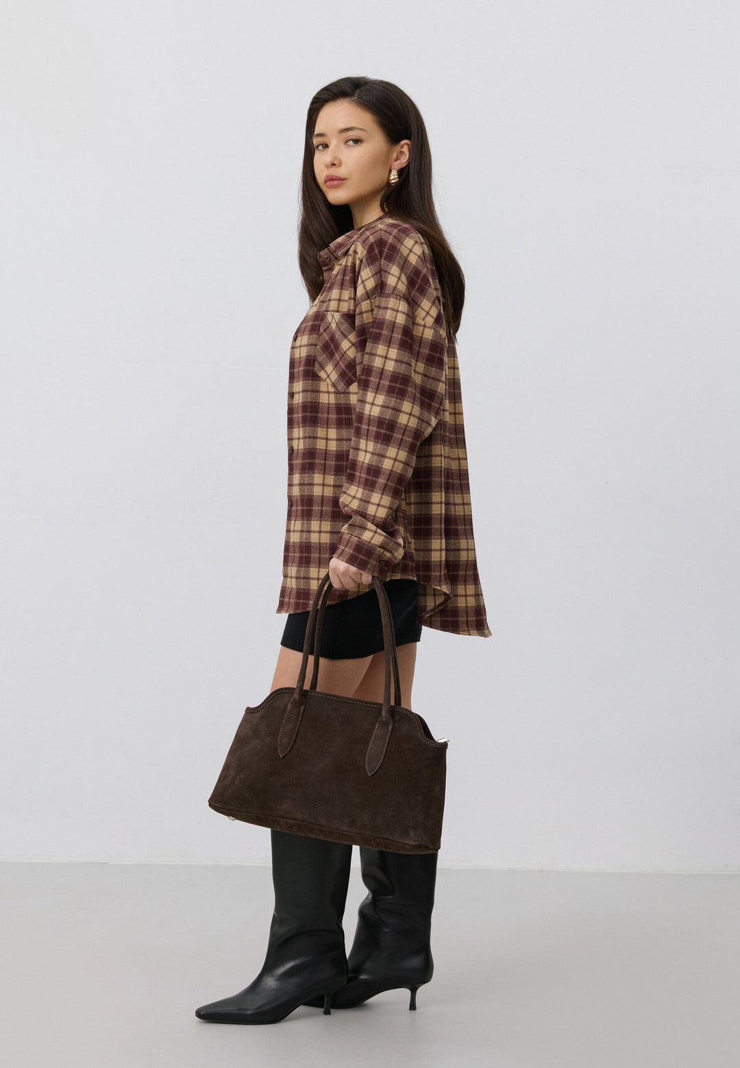 Lifestyle-Aufnahme einer Frau im karierten Hemd, die die dunkelbraune Velours-Schultertasche elegant in der Hand präsentiert