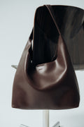 Stilvolle Nahaufnahme der dunkelbraunen Damen-Shopper-Tasche aus geschmeidigem Echtleder mit dezenter Logo-Prägung, elegant über eine Stuhllehne drapiert