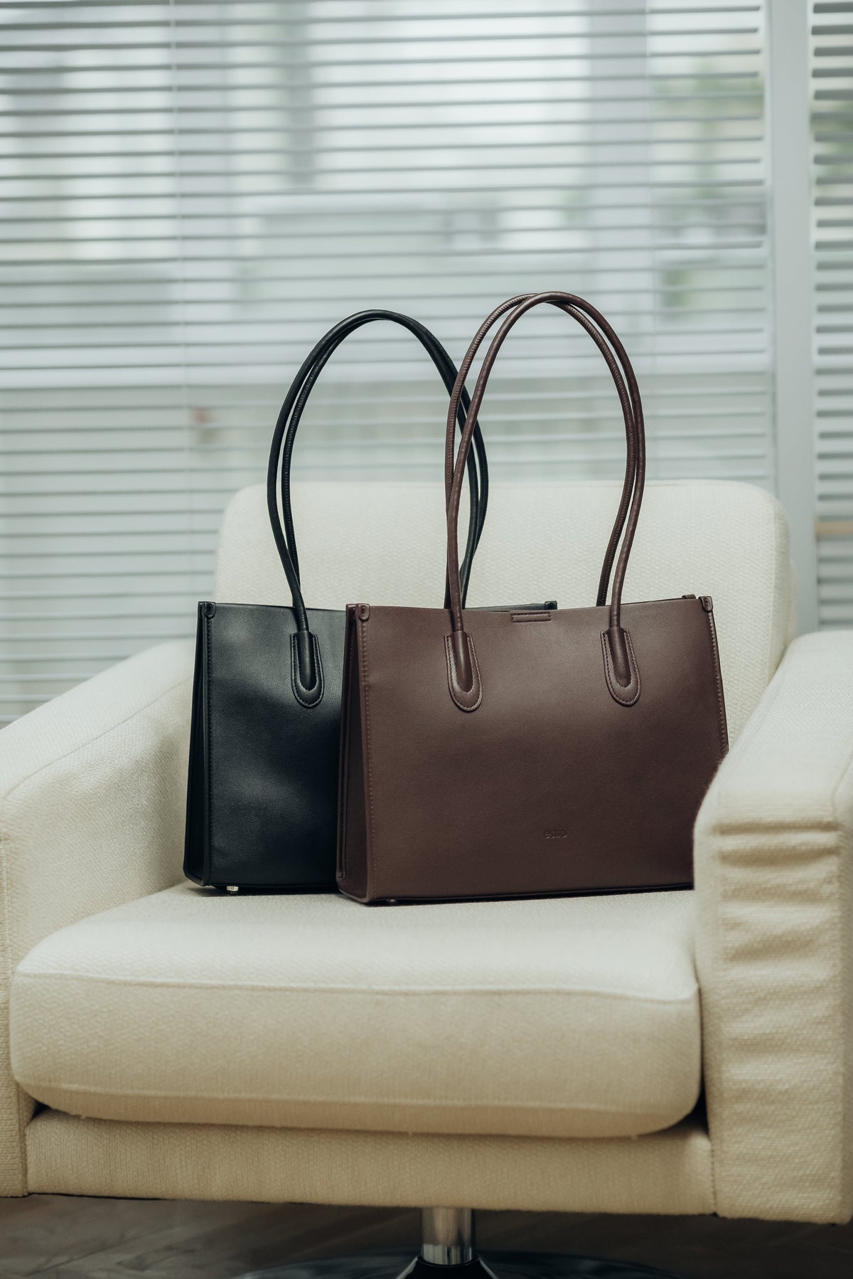 Dunkelbraune und schwarze Damen-Shopper-Tasche aus Leder, stilvoll auf einem hellen Sessel arrangiert