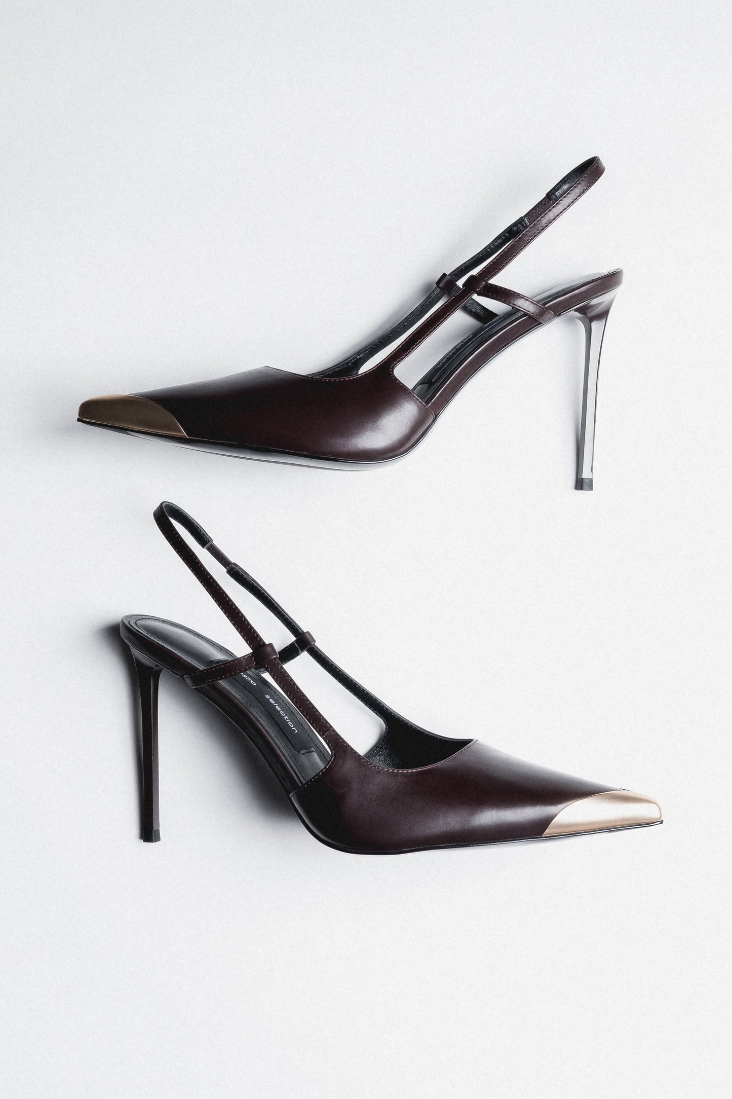 Dunkelbraune Damen-Slingpumps aus Leder als Paar in schräger Seitenansicht mit goldfarbener Spitze