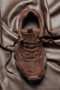Draufsicht auf braune Chunky-Sneaker aus Veloursleder mit Mesh-Einsätzen und strukturierter Sohle auf einem Ledertuch