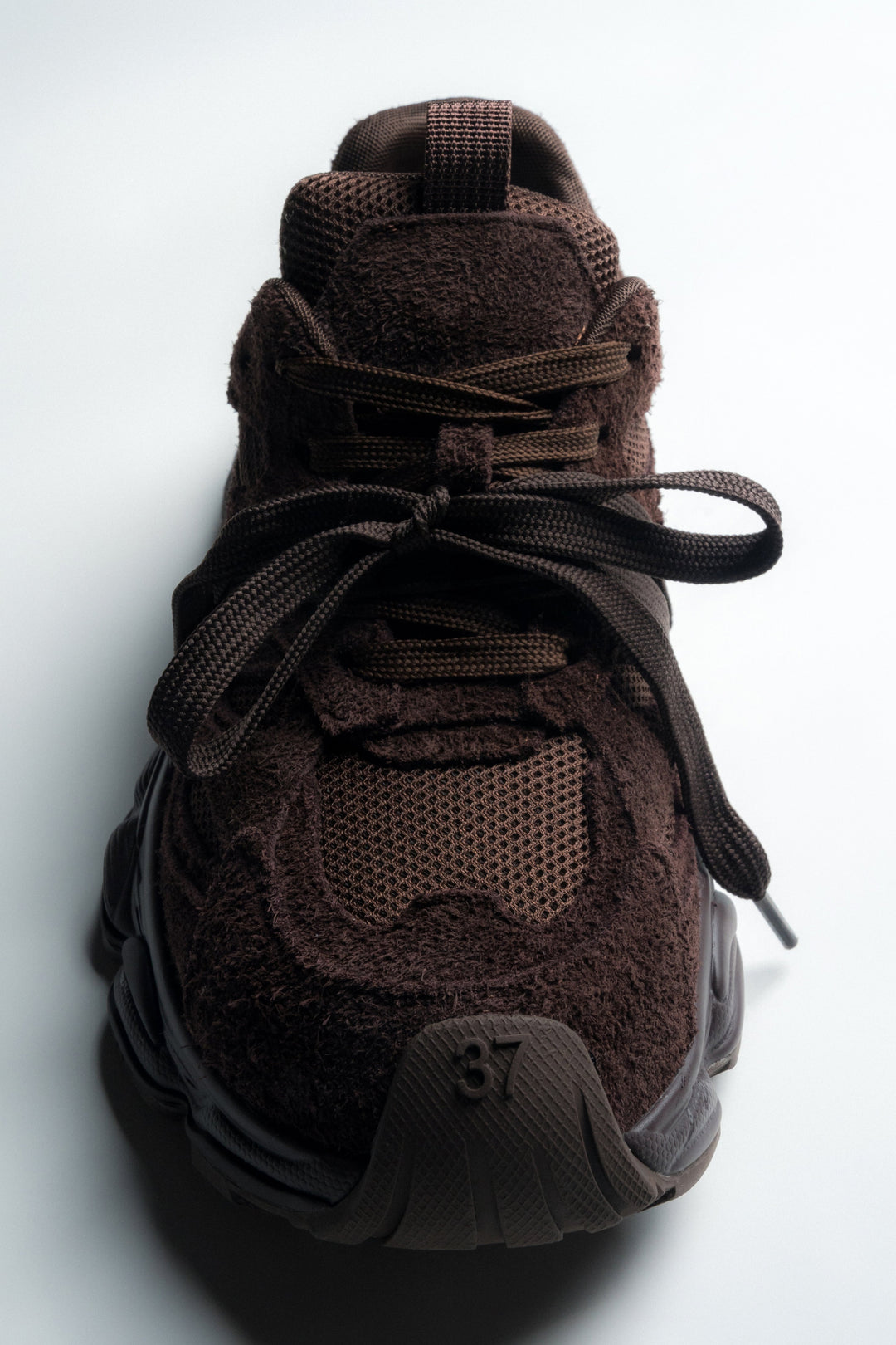 Frontalansicht des dunkelbraunen Sneakers mit Fokus auf die runde Schuhspitze und Textur
