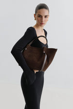 Model in schwarzem Strickkleid trägt die dunkelbraune Velours-Tasche in Boot-Form unter dem Arm
