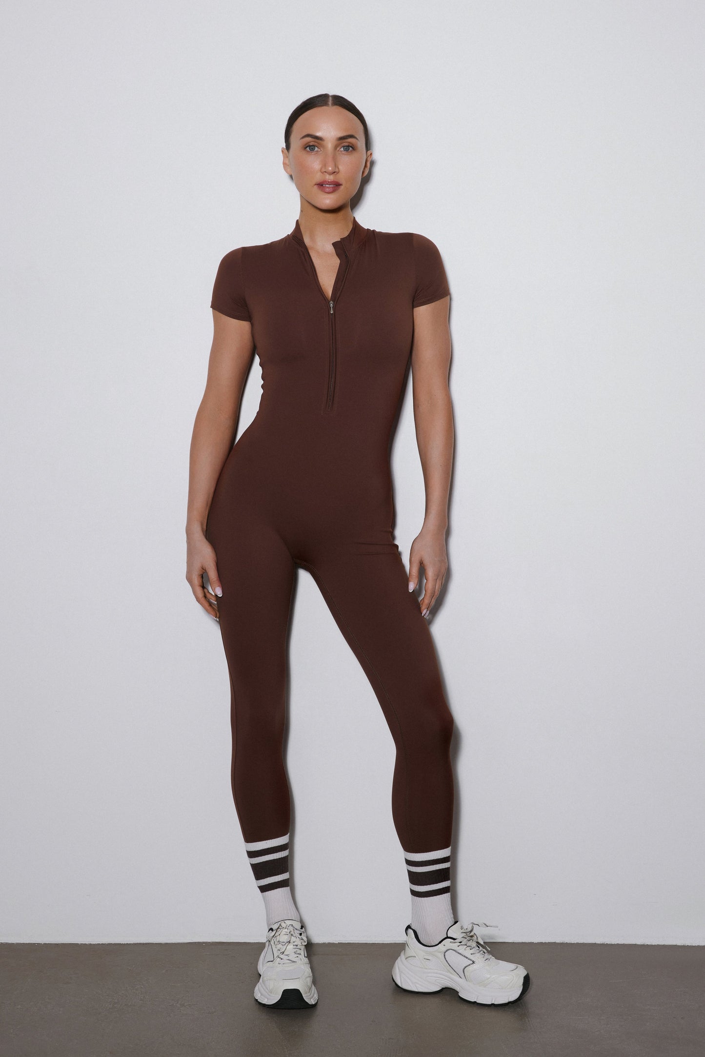 Ganzkörper-Vorderansicht: Dunkelbrauner Sport-Jumpsuit für Damen mit kurzen Ärmeln und langen Hosenbeinen.