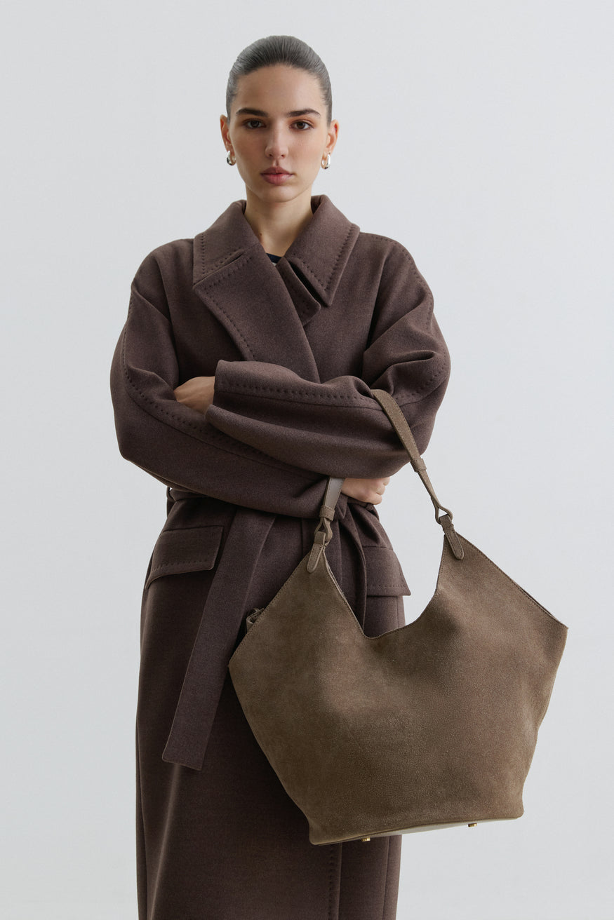 Model im braunen Mantel mit der dunkelgrauen Hobo-Tasche aus Naturvelours über der Schulter 