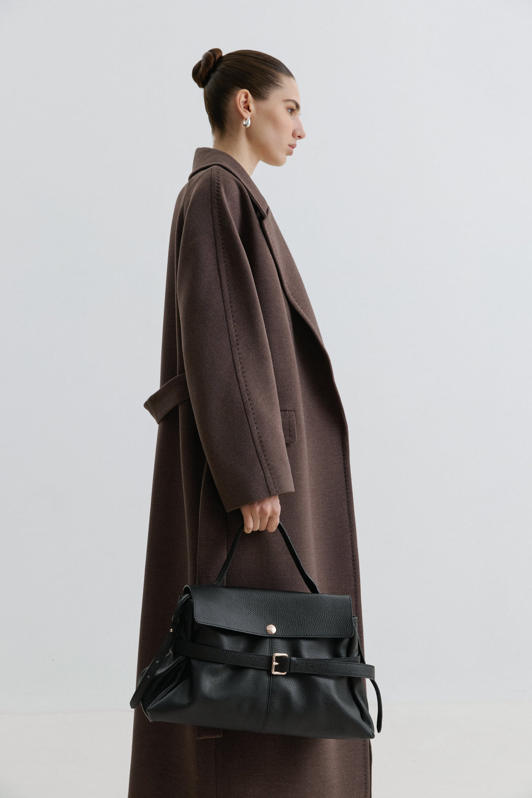 Model in einem braunen Mantel präsentiert die schwarze Henkeltasche in der Hand