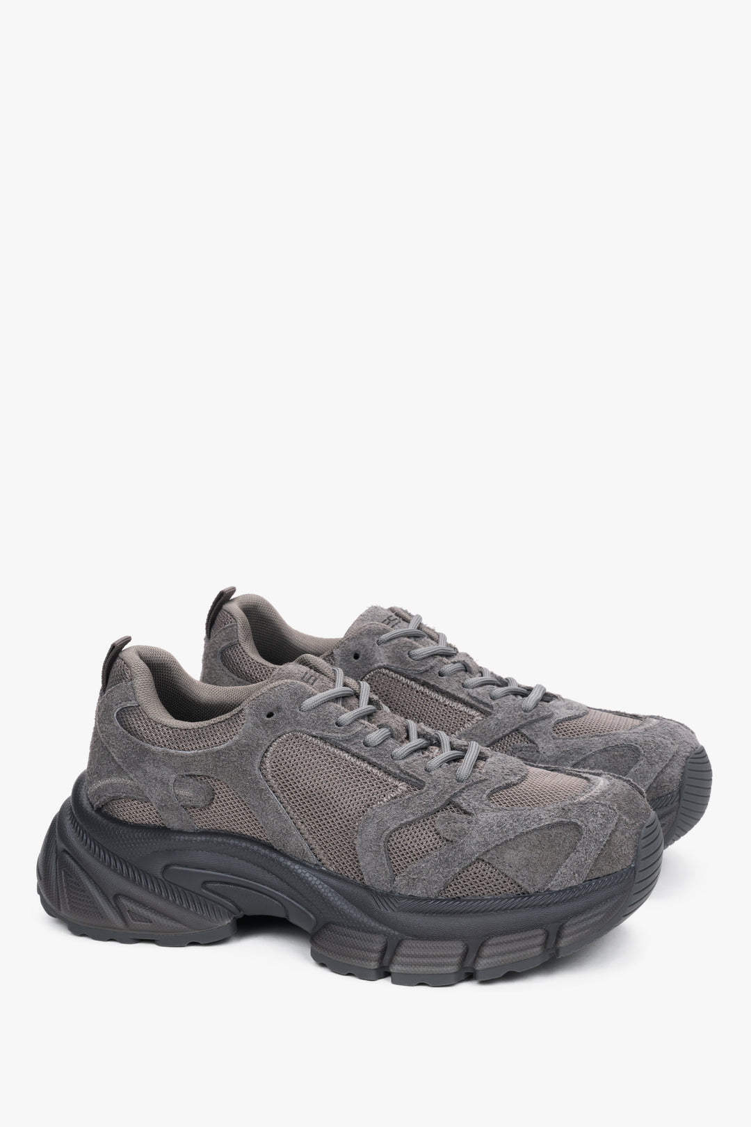 Frontale Schrägansicht des grauen Sneaker-Paares mit Fokus auf die abgerundete Schuhspitze, den strukturierten Materialmix und die klobige Sohle 