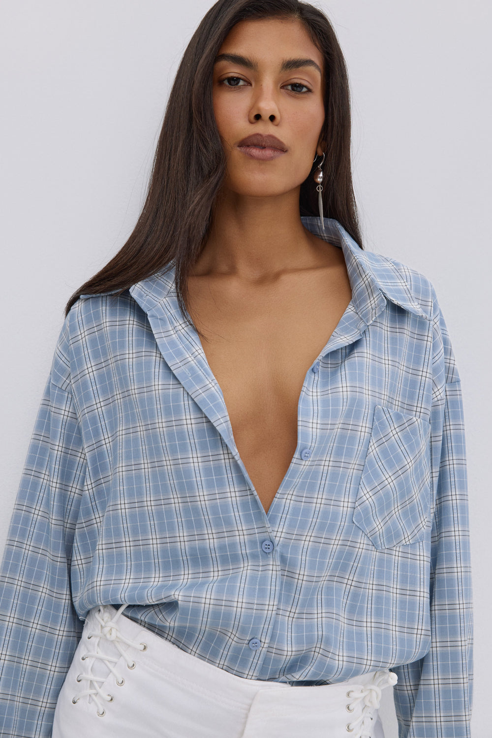 Nahaufnahme des Models in der leicht geöffneten, hellblau-weiß karierten Oversize-Hemdbluse
