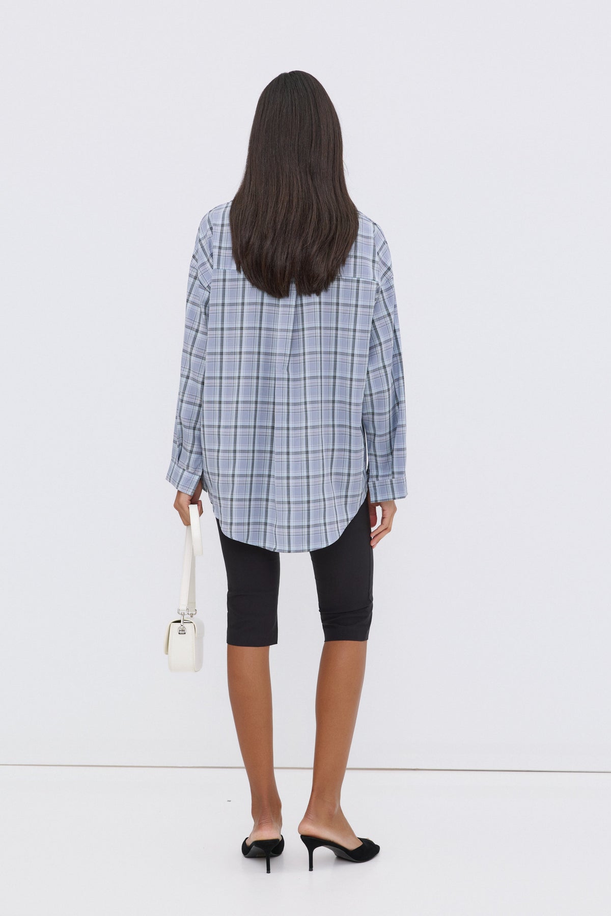 Rückansicht des Models in der verlängerten, hellblau karierten Oversize-Hemdbluse