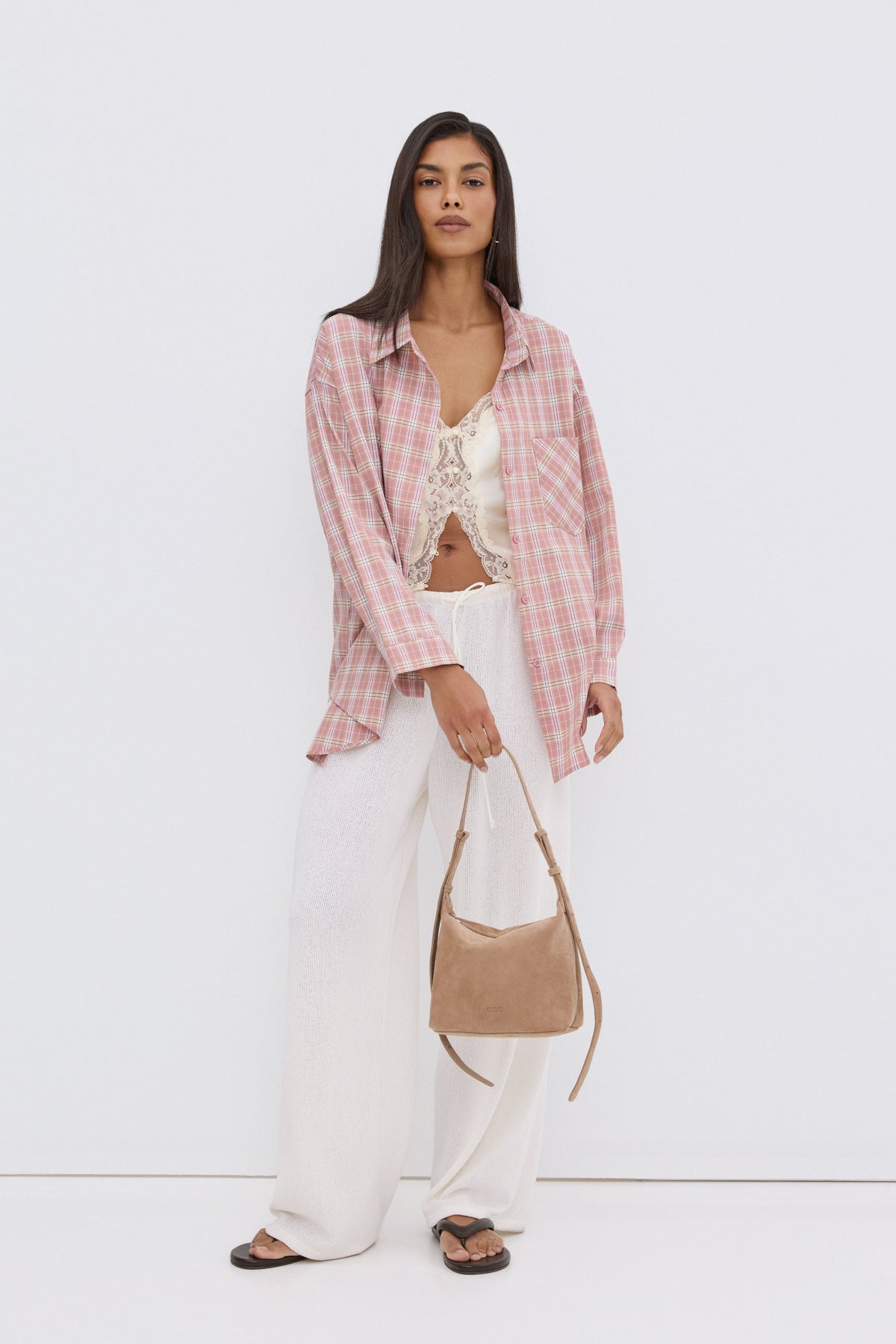 Model in leger geöffneter rosa Karo-Hemdbluse, trägt eine kleine braune Handtasche