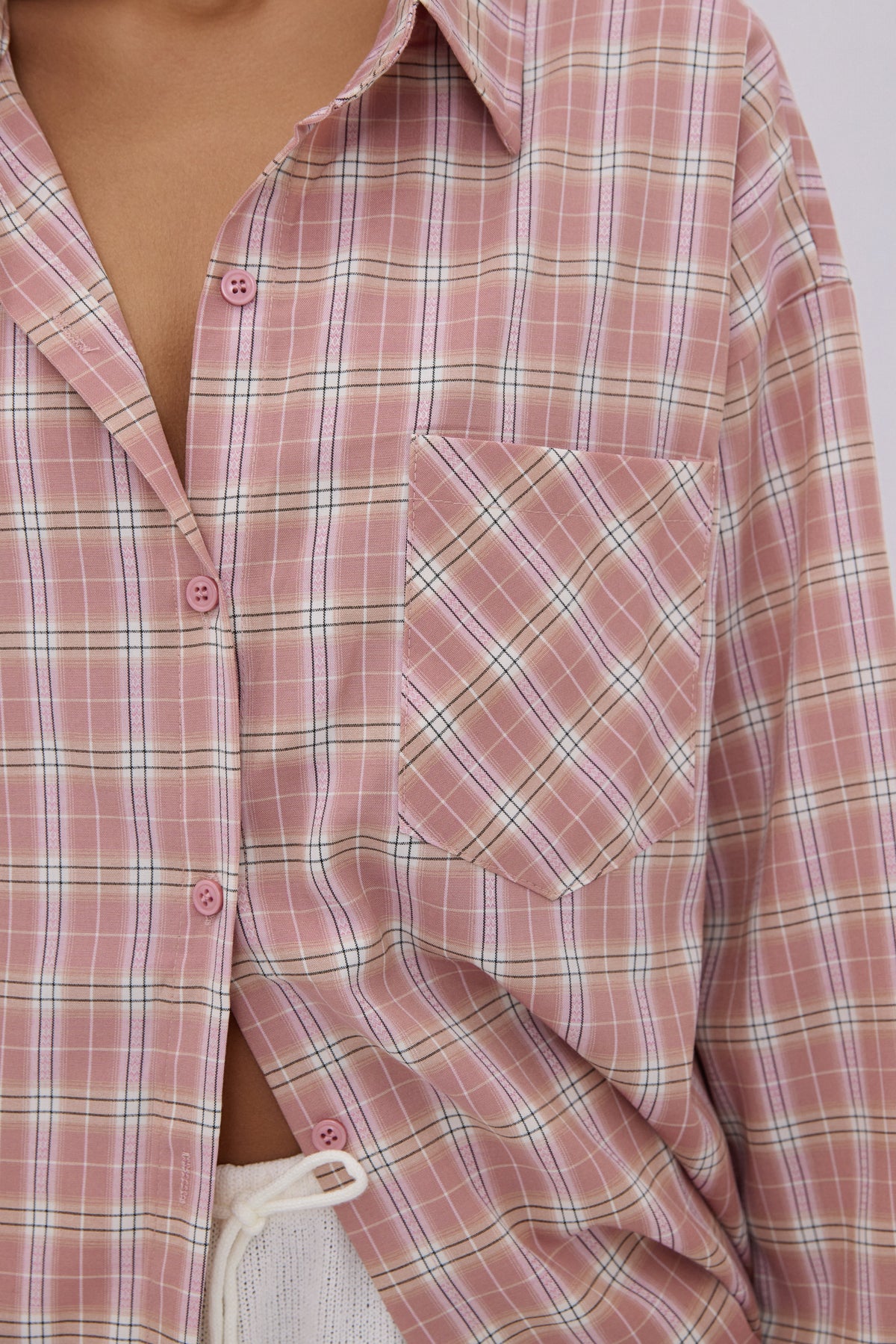Detailaufnahme des pastellfarbenen Karomusters und der Brusttasche der hellrosa Bluse
