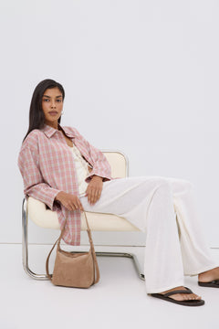Model sitzt entspannt auf einem Sessel und präsentiert die lässige Oversize-Passform der rosa Hemdbluse