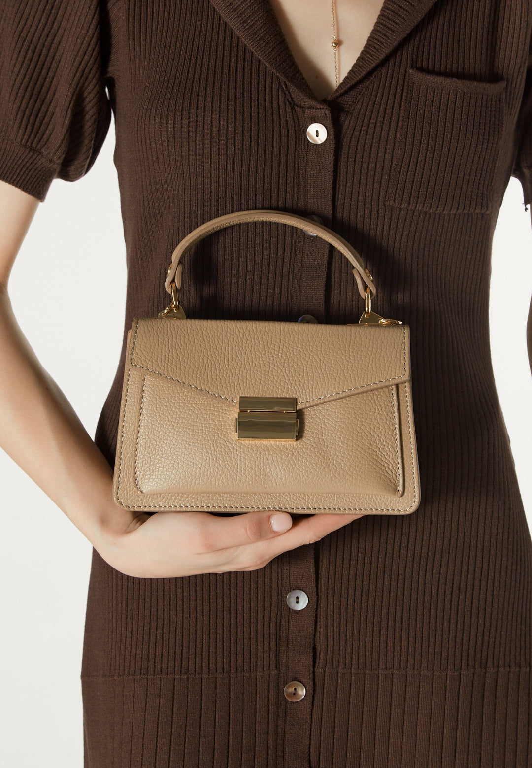 Model hält die beige Premium-Tasche elegant am kurzen Henkel in der Hand 