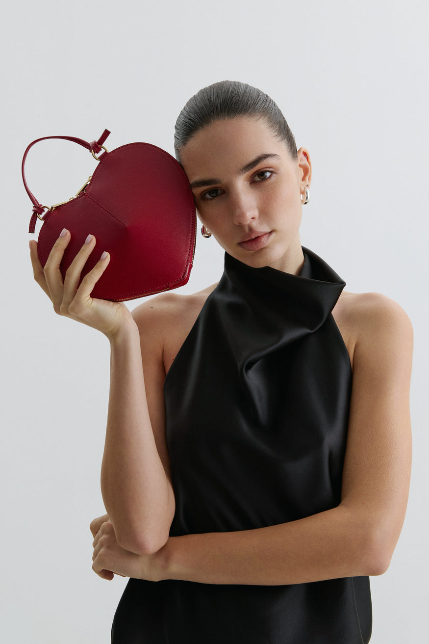 Kampagnenbild eines Models im schwarzen Top, das die rote Herz-Handtasche elegant präsentiert