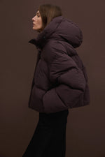 Seitenprofil des Models in der kurzen dunkelbraunen Pufferjacke mit aufgesetzter Kapuze