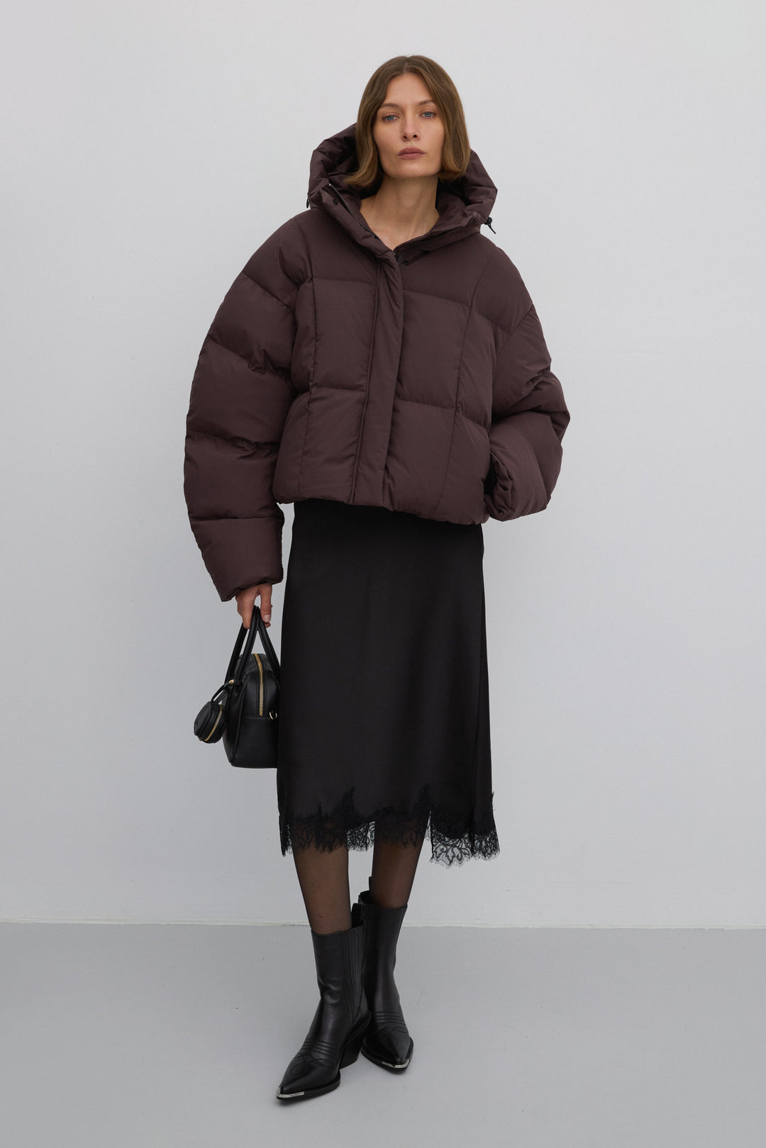 Ganzkörperaufnahme des Models in Pufferjacke, schwarzem Midirock und Lederstiefeln