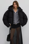 Model präsentiert die offene kurze schwarze Oversize-Pufferjacke mit Kapuze