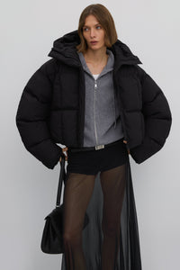 Model präsentiert die offene kurze schwarze Oversize-Pufferjacke mit Kapuze