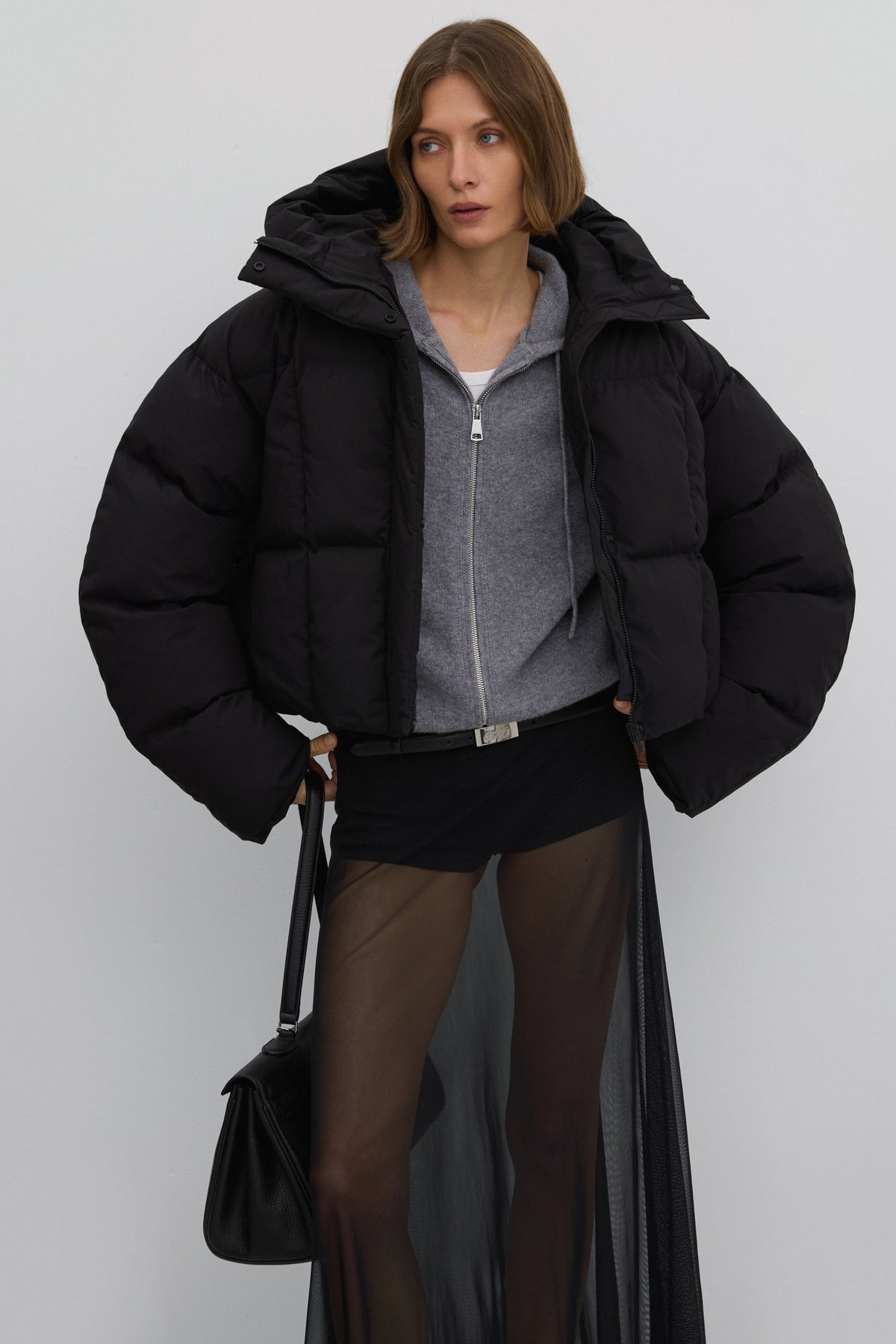 Model präsentiert die offene kurze schwarze Oversize-Pufferjacke mit Kapuze