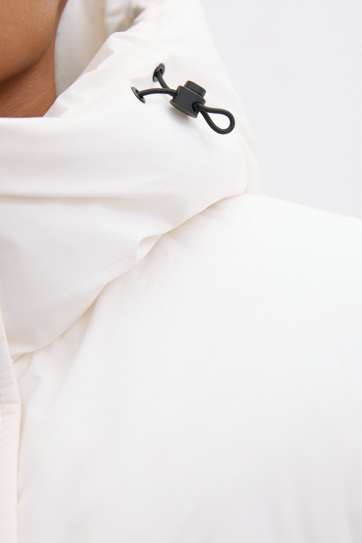 Detailaufnahme des hohen Stehkragens und der Kapuze der milchbeigen Pufferjacke mit Kordelzug 
