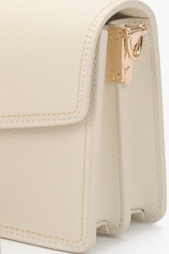 Detailaufnahme der goldenen Beschläge an der hellbeigen Ledertasche.