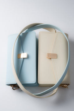 Draufsicht auf die milchbeigen und hellblauen Ledertaschen mit Trageriemen.