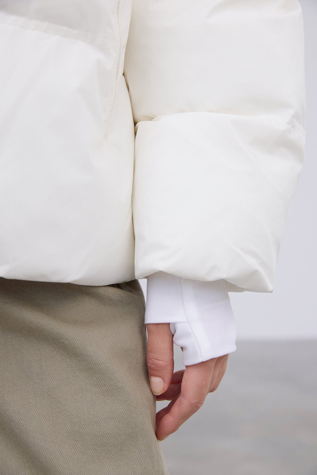 Detailaufnahme des Ärmels der milchbeigen Pufferjacke mit Fokus auf das verlängerte, enganliegende Bündchen 