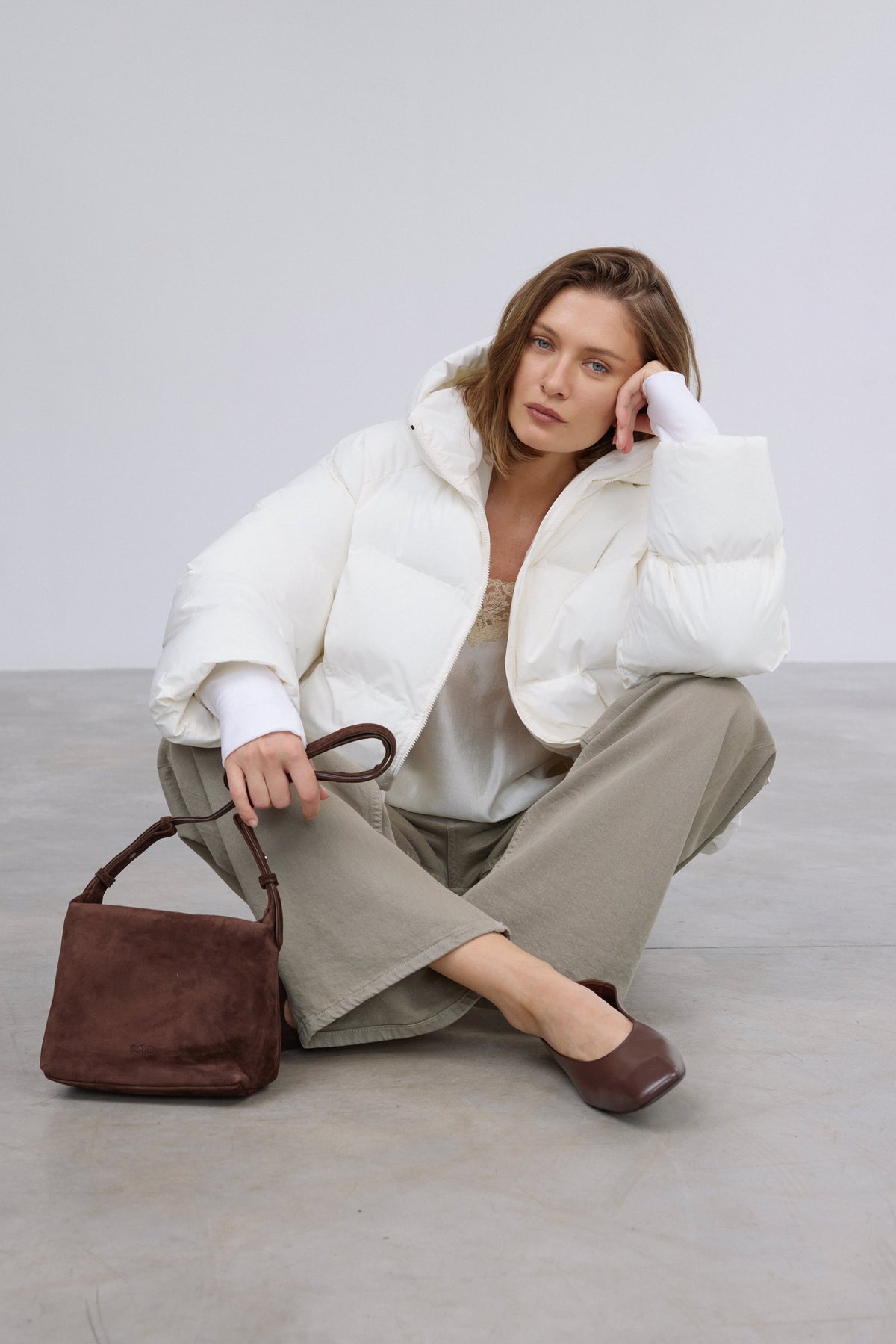Model sitzt in der geöffneten milchbeigen Winterjacke, was die bequeme Passform und Bewegungsfreiheit demonstriert 