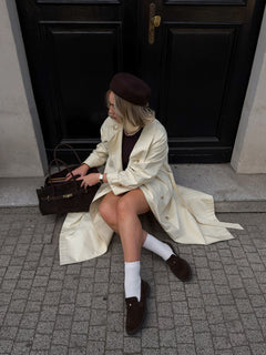 Model im hellen Mantel und mit Baskenmütze trägt die dunkelbraunen Velours-Loafer mit weißen Socken