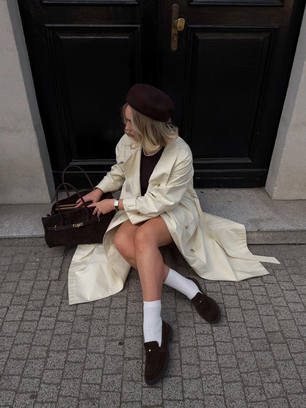 Model im hellen Mantel und mit Baskenmütze trägt die dunkelbraunen Velours-Loafer mit weißen Socken