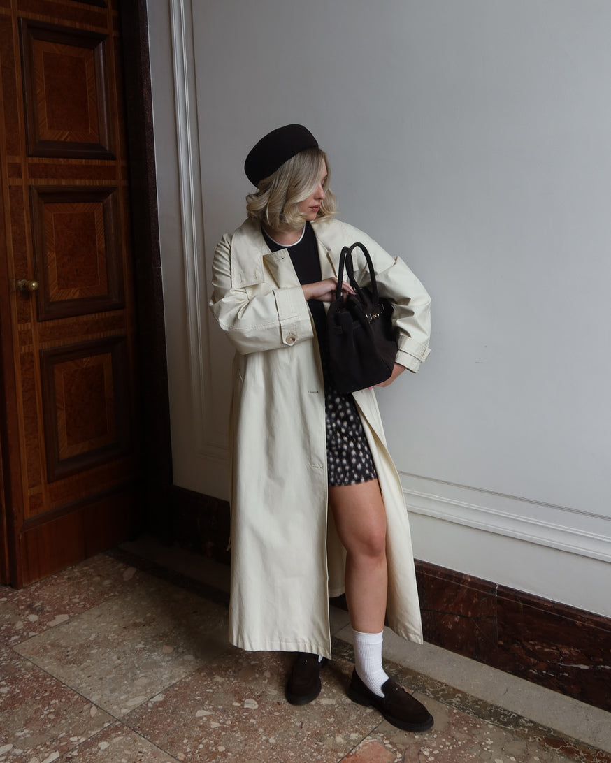 Model steht im cremefarbenen Mantel und präsentiert die klassischen dunkelbraunen Loafer