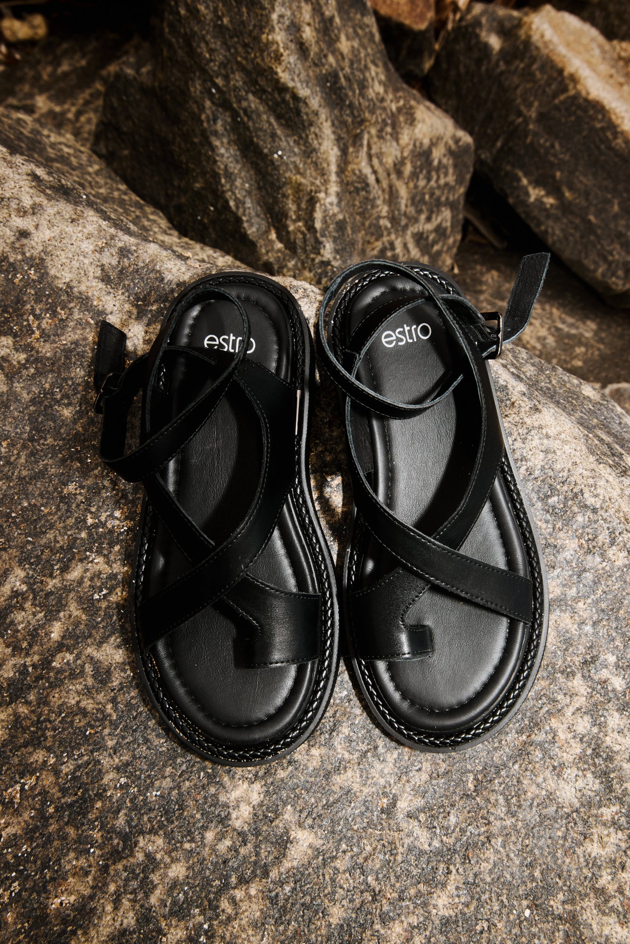 Draufsicht auf das Paar schwarzer Sandalen von Estro am Stein
