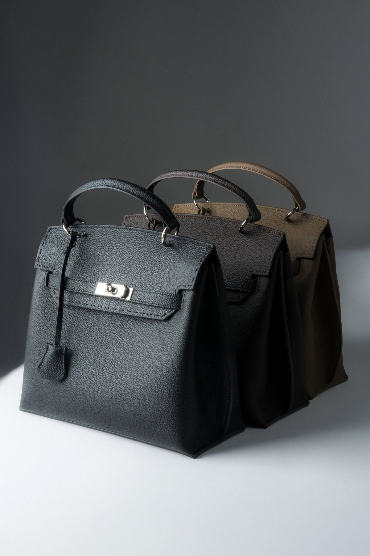 Draufsicht auf drei Varianten der Estro Henkeltasche in Schwarz, Dunkelbraun und Khaki.