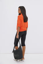 Model in Seitenansicht mit orangefarbenem Oberteil, trägt die schwarze Echtleder-Hobo-Tasche lässig in der Hand