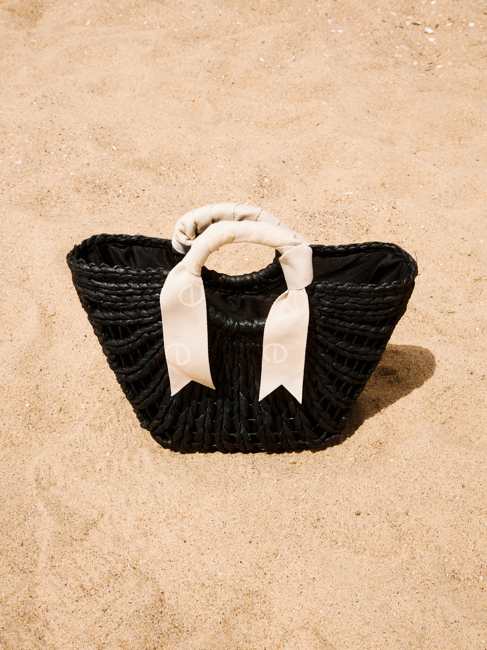 Stilvolle schwarze geflochtene Damen Korbtasche mit kontrastierendem weißem Schleifen-Henkel am Strand