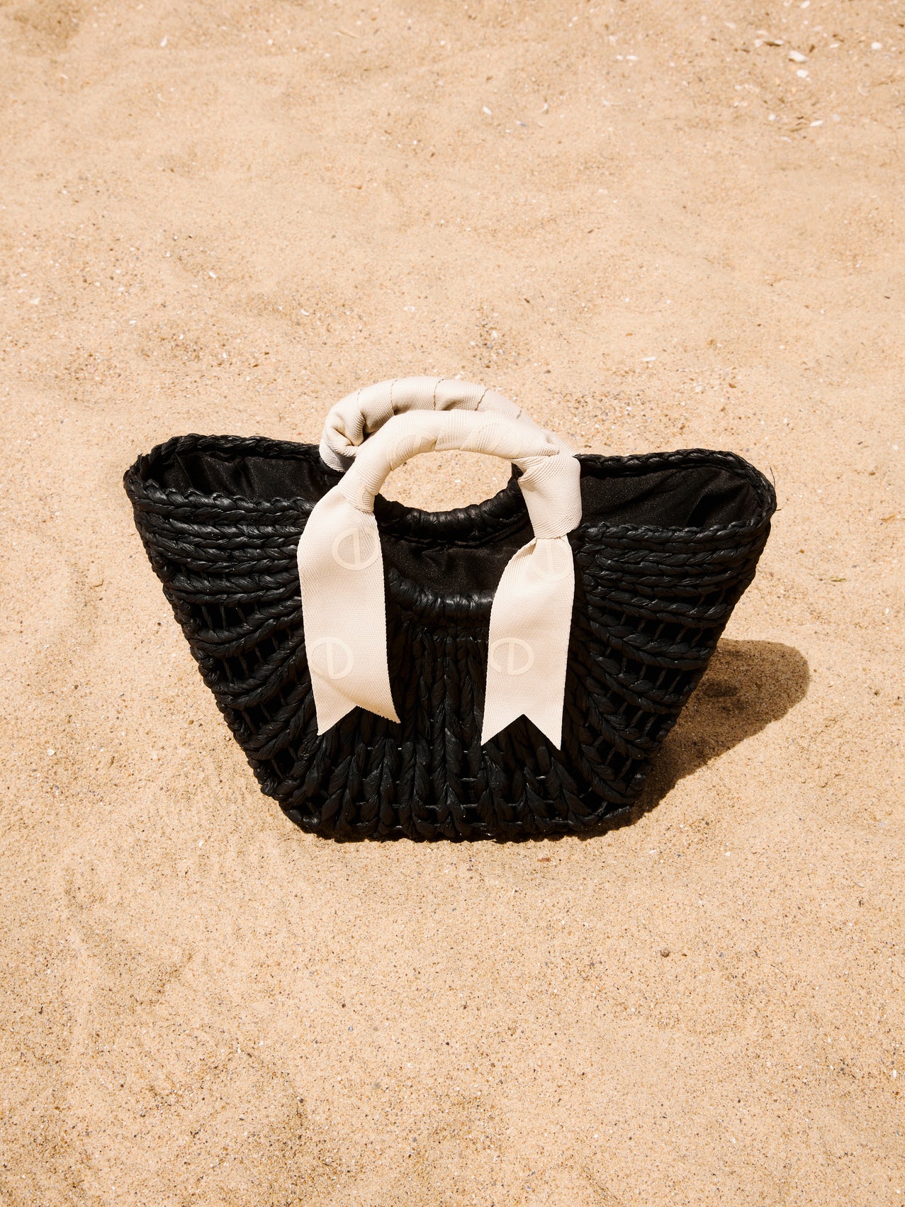Stilvolle schwarze geflochtene Damen Korbtasche mit kontrastierendem weißem Schleifen-Henkel am Strand