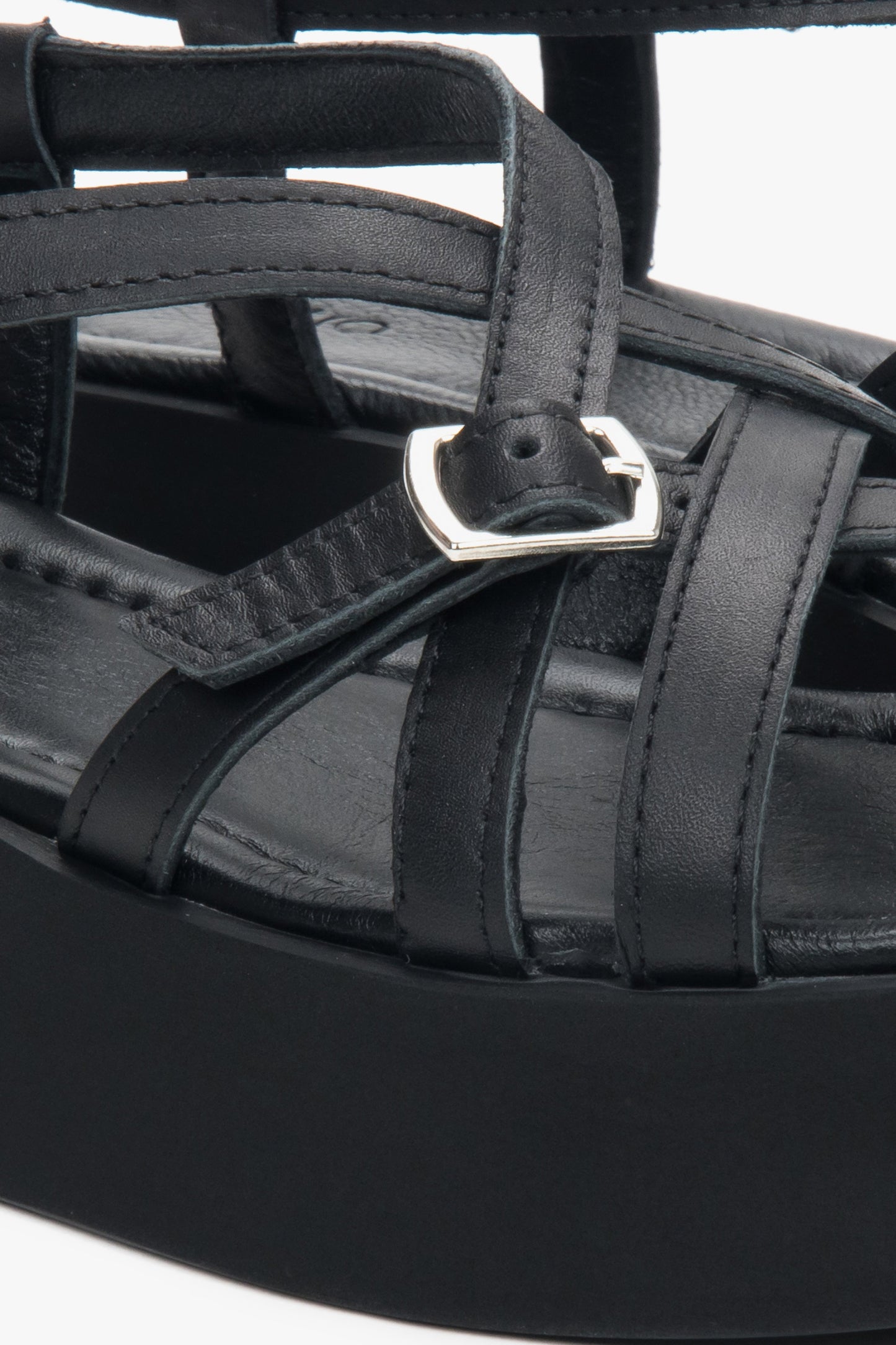 Detailaufnahme der silbernen Schnalle und der Lederriemen an den schwarzen Plateau-Sandalen