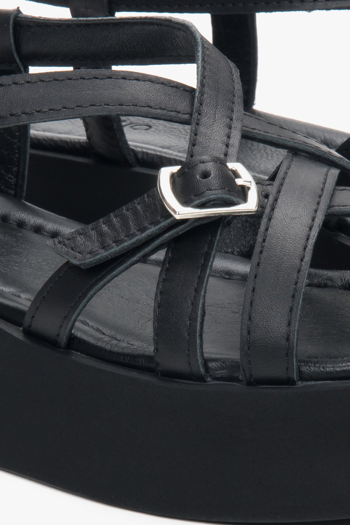 Detailaufnahme der silbernen Schnalle und der Lederriemen an den schwarzen Plateau-Sandalen