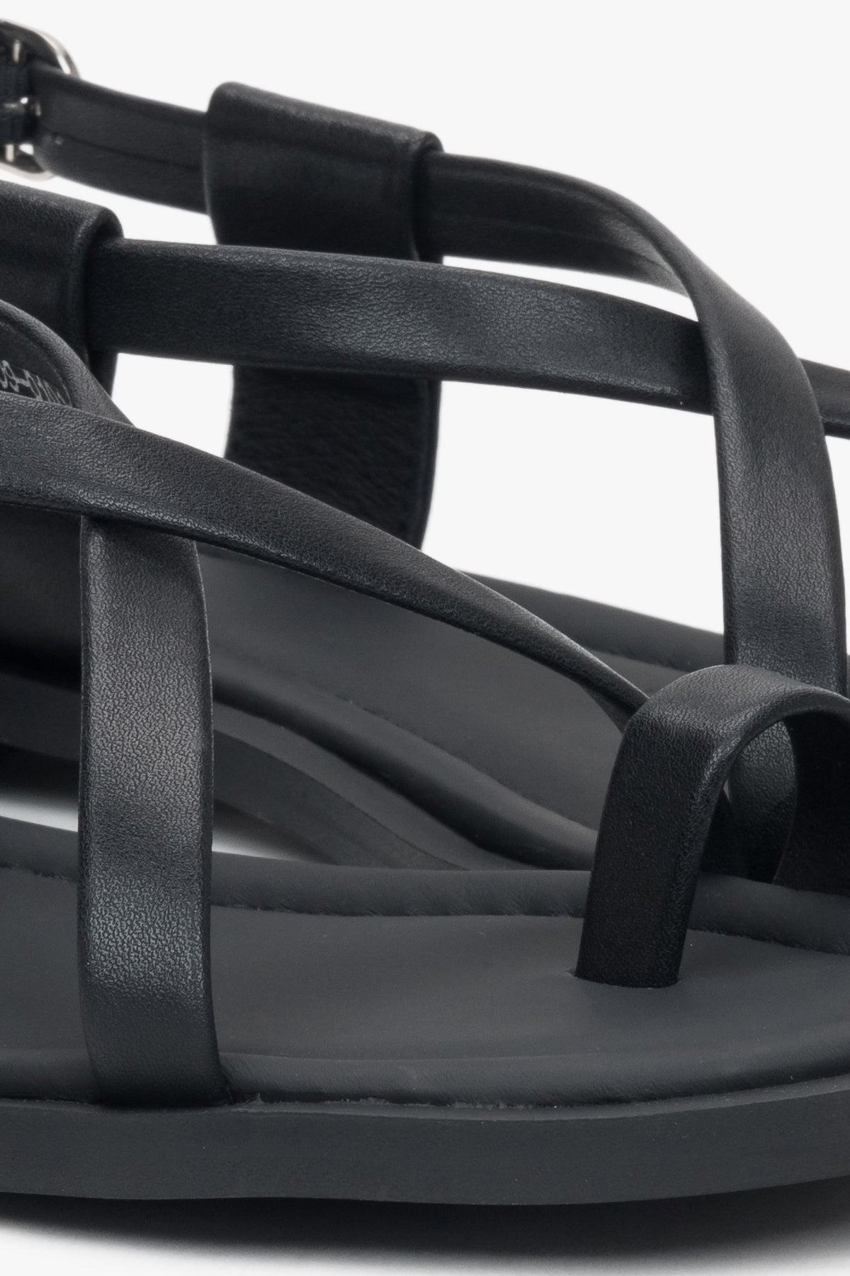 Nahaufnahme der dekorativen Zehenschlaufe und Riemen der schwarzen Damen-Sandalen.
