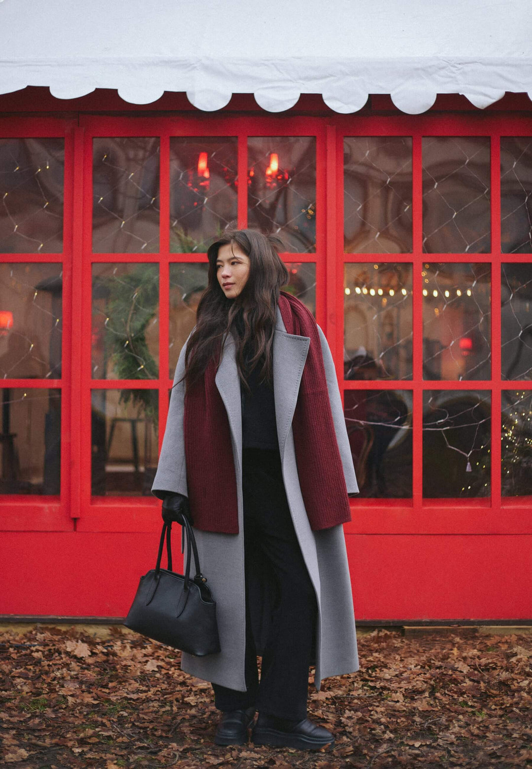 Lifestyle-Aufnahme einer Frau im Herbstmantel, die die schwarze Schultertasche in der Hand trägt