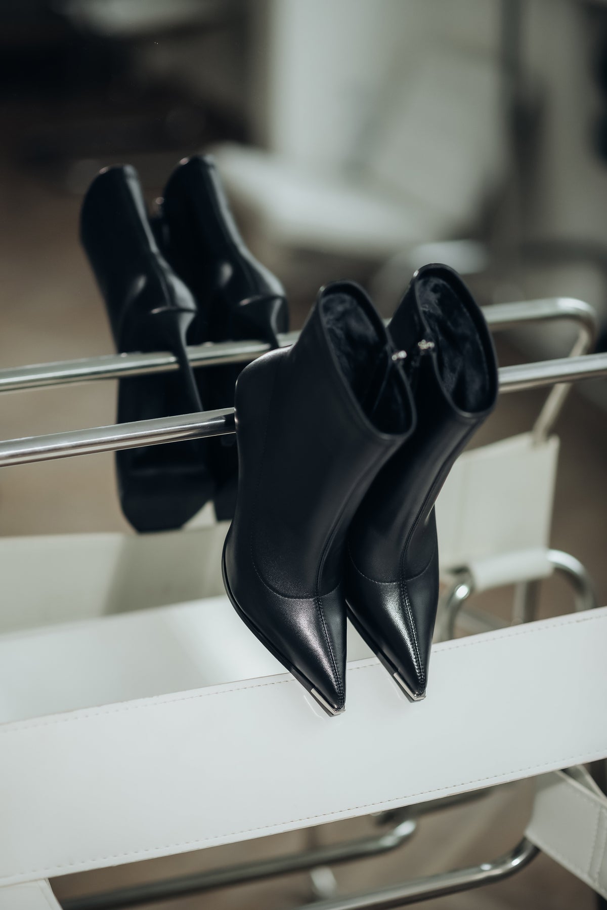 Stilvoll arrangiertes Paar schwarzer Damen-High-Heel-Boots auf einem modernen weißen Designerstuhl