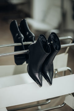 Stilvoll arrangiertes Paar schwarzer Damen-High-Heel-Boots auf einem modernen weißen Designerstuhl