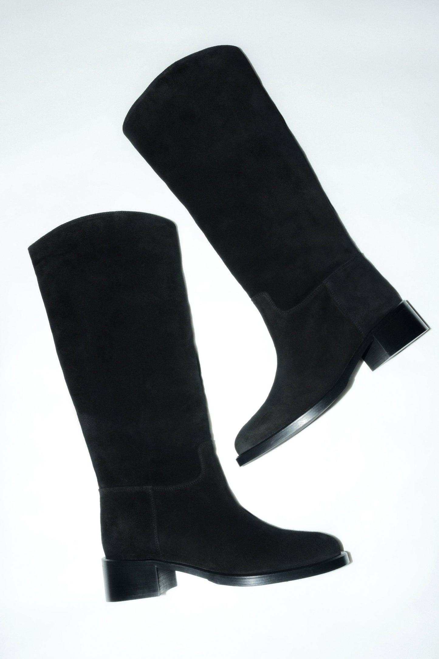 Künstlerische Draufsicht des schwarzen Veloursstiefel-Paares auf hellem Untergrund 