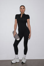 Ganzkörperansicht des schwarzen Damen-Sport-Jumpsuits mit kurzen Ärmeln und langen Beinen von vorne.